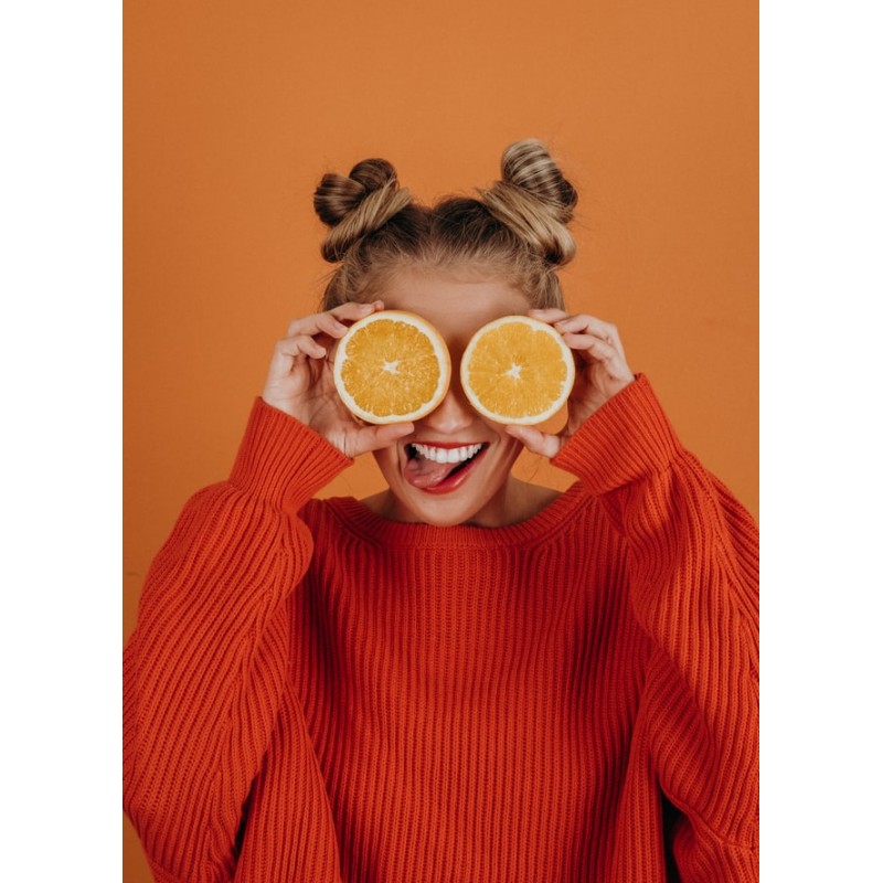 Femme tenant deux tranches d\'orange devant ses yeux en tirant la langue