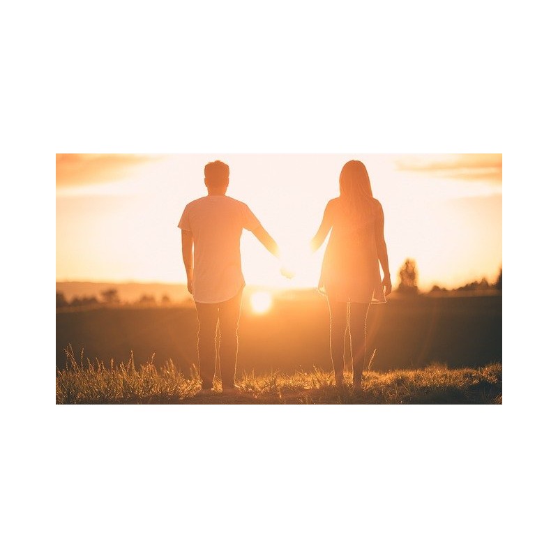 Couple se tenant la main face à un coucher de soleil.
