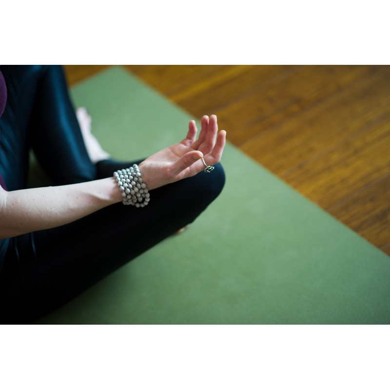 Femme en posture de méditation assise sur un tapis de yoga vert