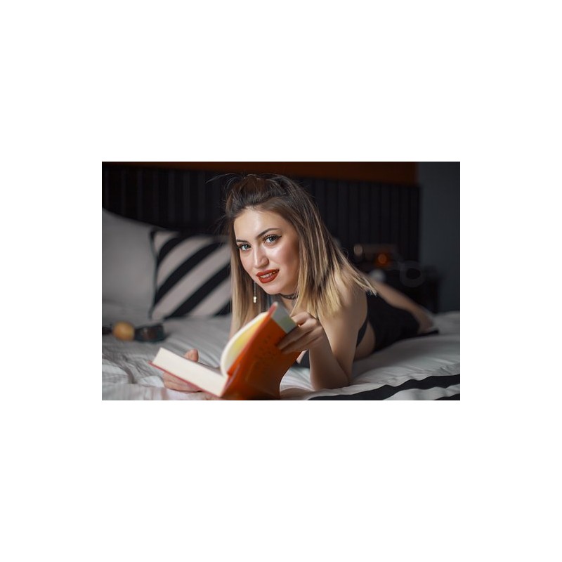 Une femme allongée sur un lit et qui tient un livre