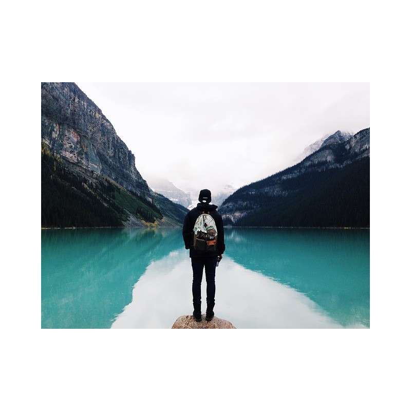 un touriste vu de dos face à un lac de montagne
